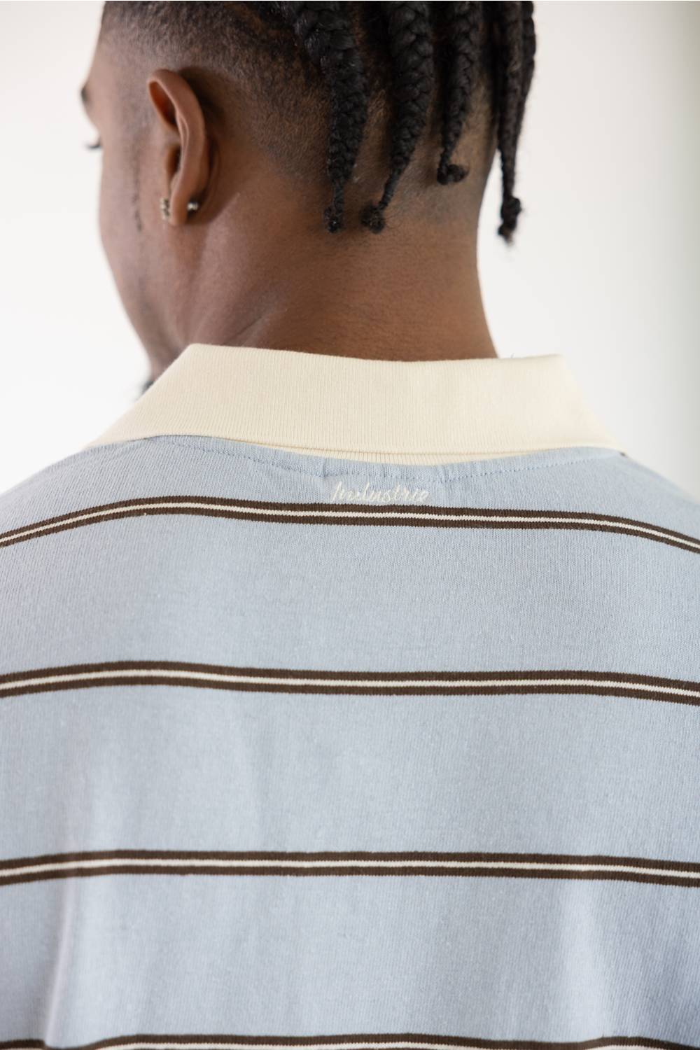 Close-up back view of a person wearing a light blue striped polo shirt with a cream collar and thin brown horizontal stripes.