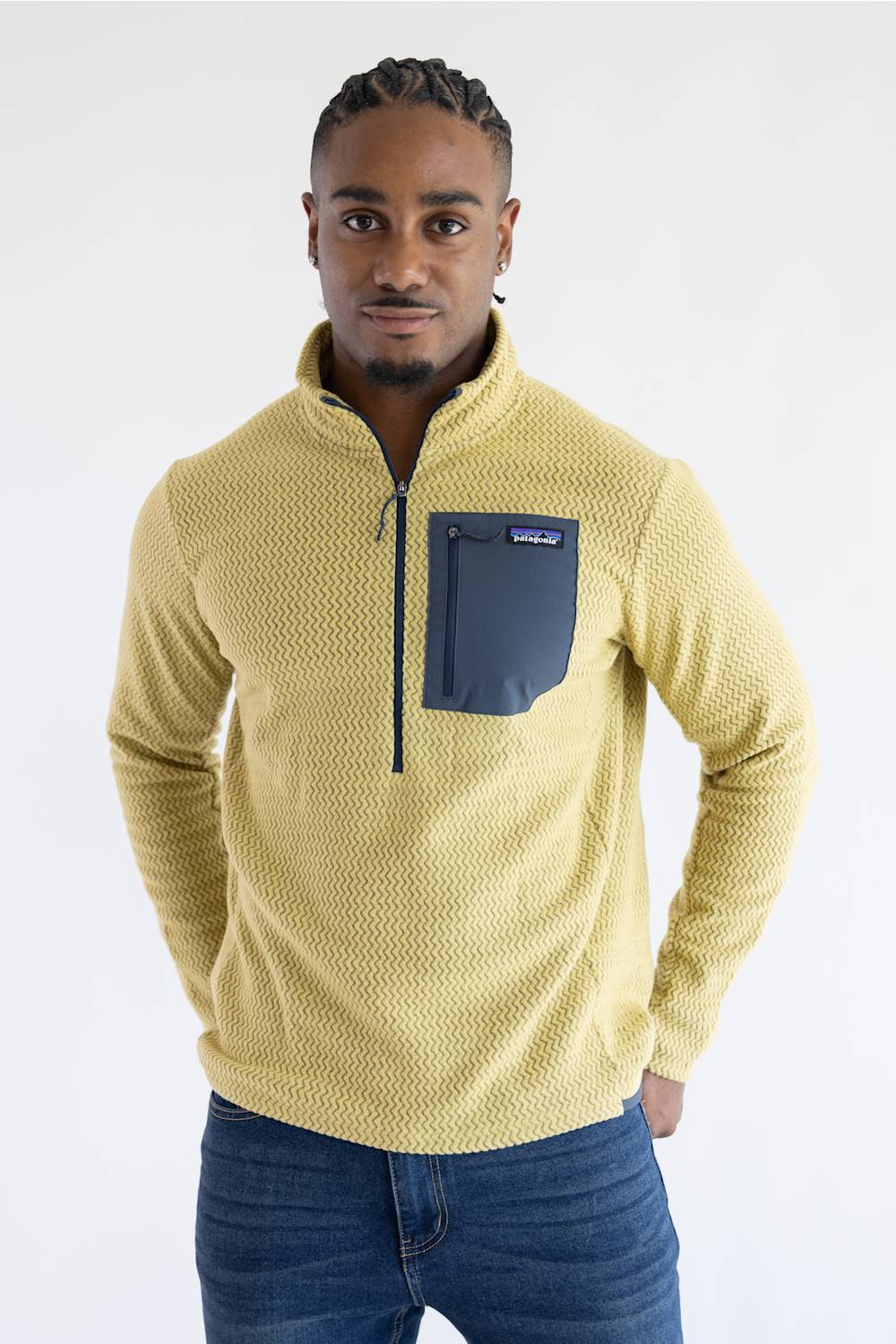 A man wearing a textured yellow quarter-zip pullover sweater with a dark navy chest pocket, paired with blue jeans, against a plain white studio background.