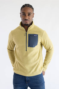 A man wearing a textured yellow quarter-zip pullover sweater with a dark navy chest pocket, paired with blue jeans, against a plain white studio background.