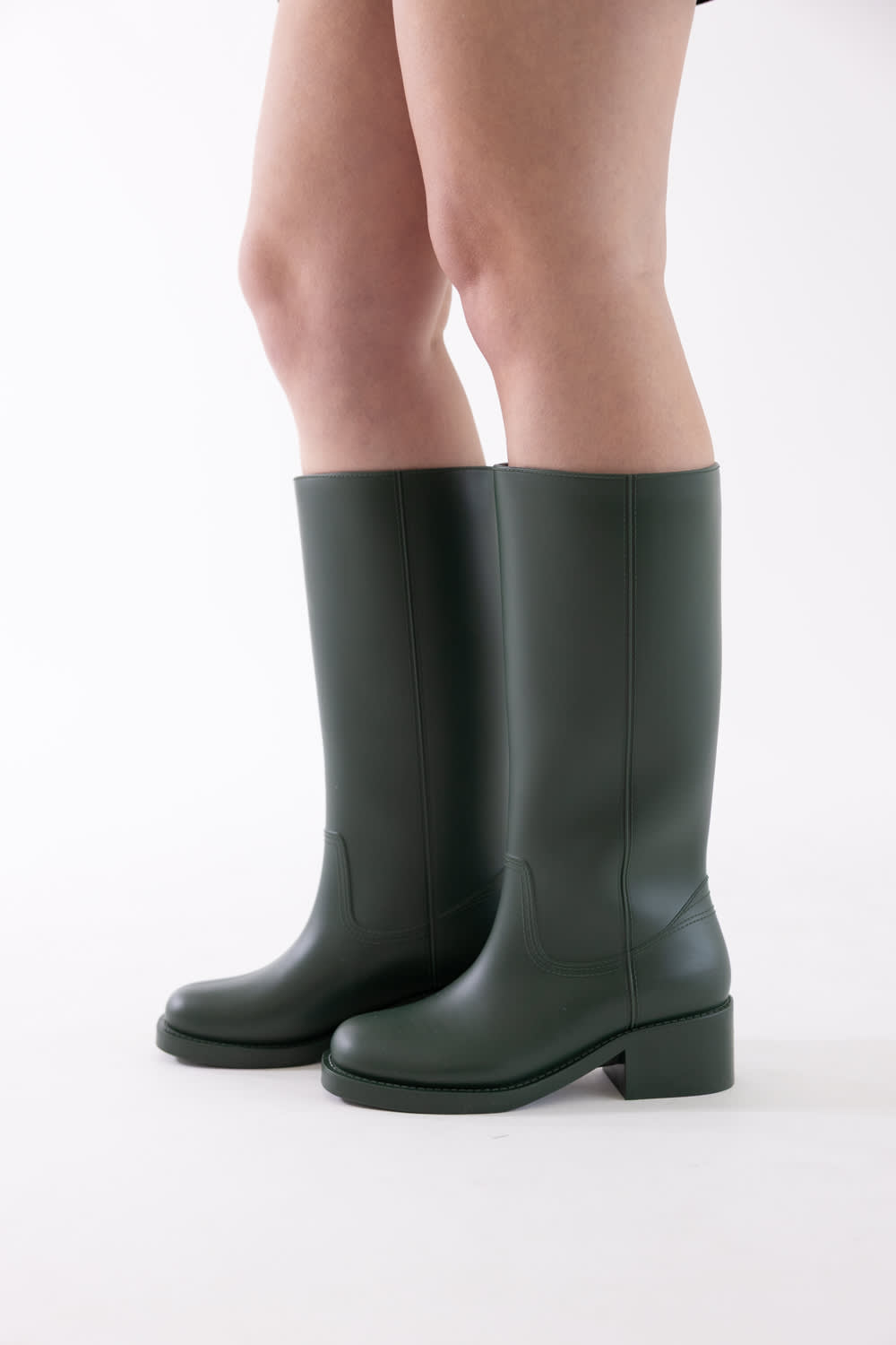 Dark green knee-high leather boots with low block heels, shown on a model's feet against a plain white studio background.