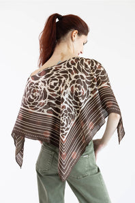 A woman with red hair tied back is shown from behind wearing a brown and beige patterned scarf draped over her shoulders, paired with olive green pants, against a plain white background.