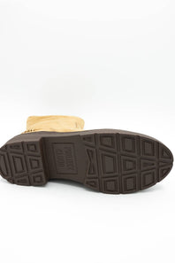 A close-up shot of the sole of a boot, showing a dark brown rubber tread with a textured geometric pattern and embossed branding, with a tan suede or fabric upper visible at the top, on a white background.