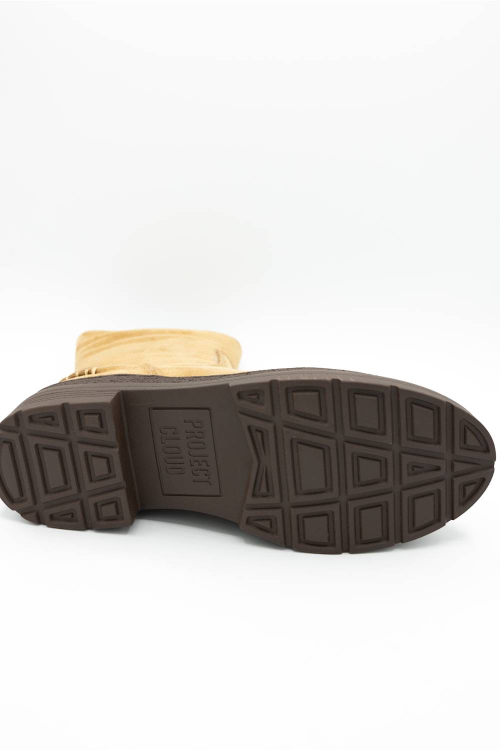 A close-up shot of the sole of a boot, showing a dark brown rubber tread with a textured geometric pattern and embossed branding, with a tan suede or fabric upper visible at the top, on a white background.