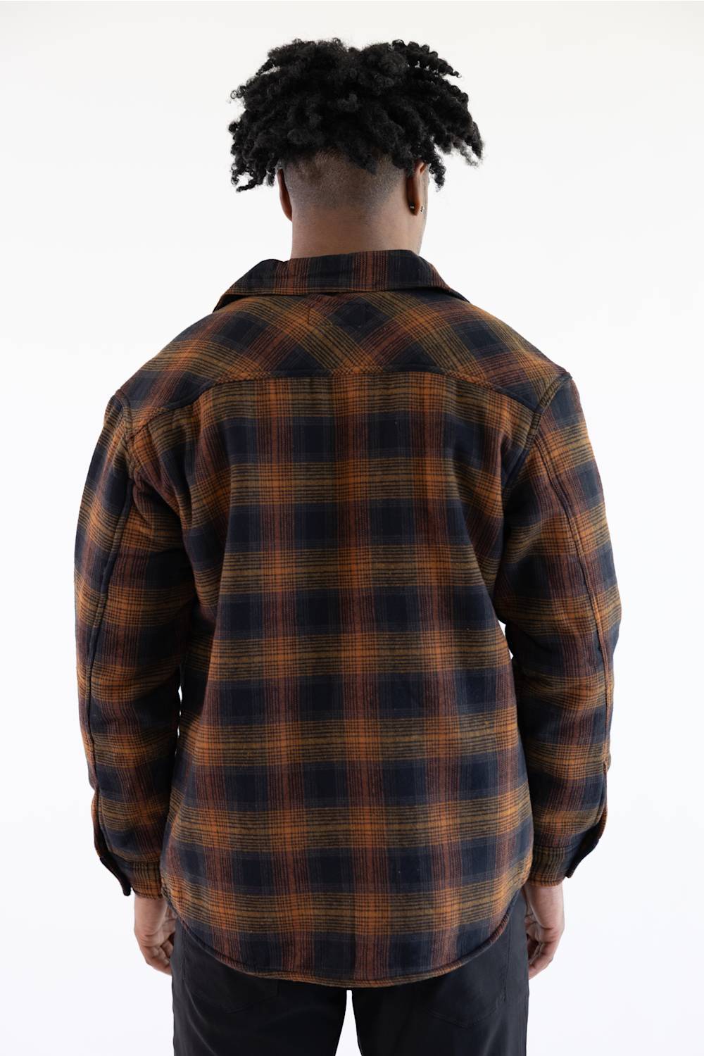 A man viewed from behind wearing a dark navy and brown plaid flannel shirt jacket, paired with black pants, against a plain white background.