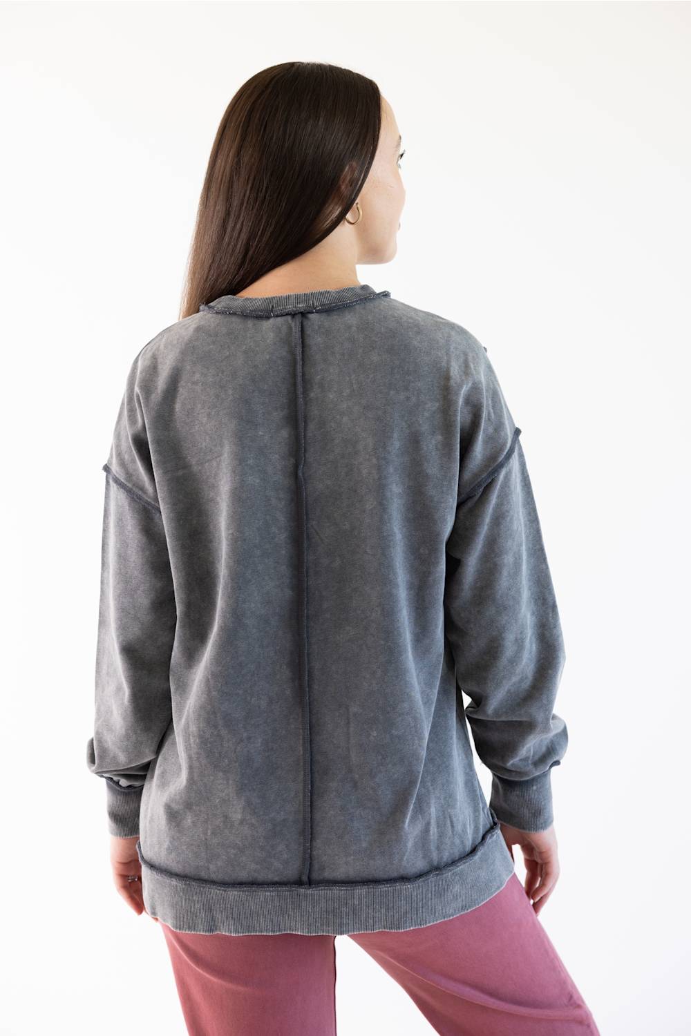 A woman viewed from the back wearing a gray long-sleeve sweatshirt and pink pants against a plain white background.