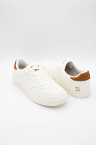 A pair of white low-top sneakers with brown heel accents and small gold logo details, photographed on a seamless white studio background.