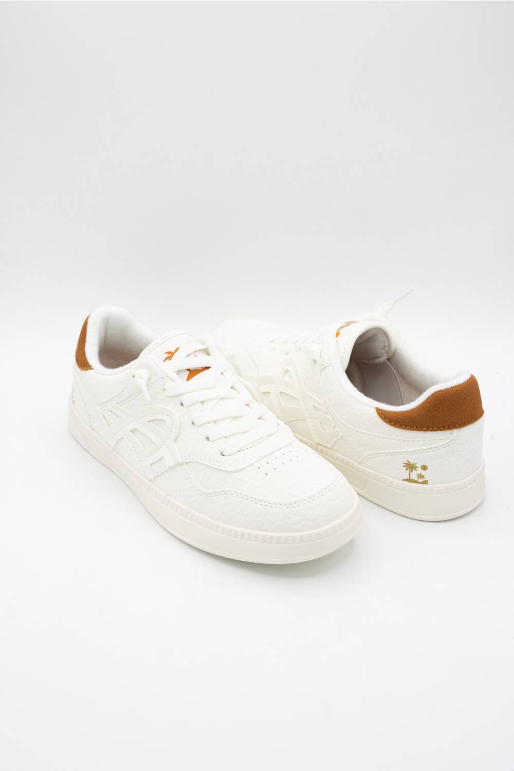 A pair of white low-top sneakers with brown heel accents and small gold logo details, photographed on a seamless white studio background.