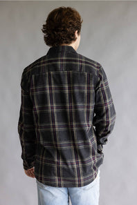 Back view of a male model wearing the Split Flannel Shirt for Men in Slate, showcasing the charcoal gray plaid pattern with burgundy and cream accent lines, straight back yoke, long sleeves, and rounded hem against a plain gray studio background.