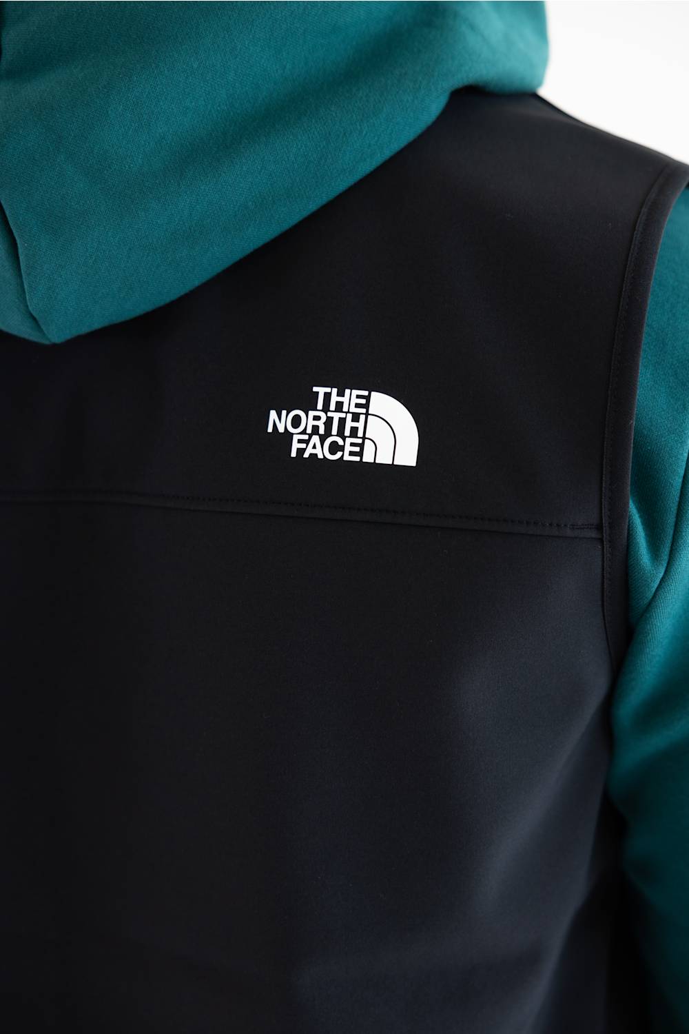 Close-up of a person wearing a black vest over a teal hoodie, with The North Face logo printed in white on the right shoulder.