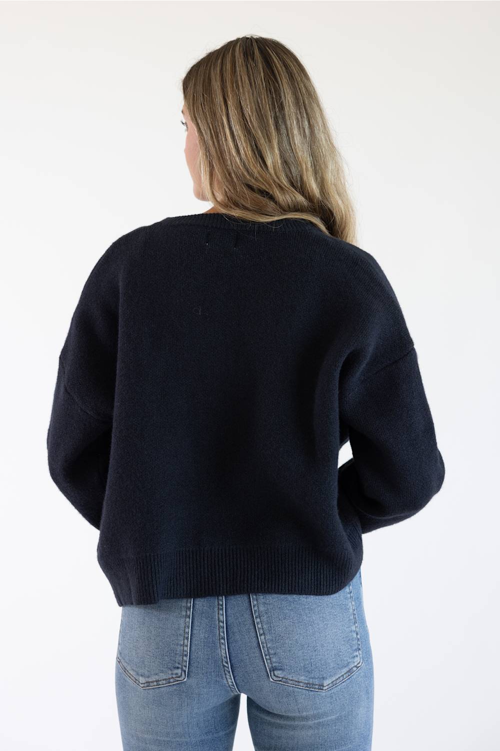 Back view of a female model wearing the Things Between Alyssa Cardigan in Navy, highlighting the drop-shoulder seam detail, relaxed fit, and ribbed hemline.