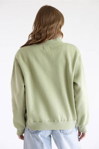 A person shown from the back wearing a light sage green sweatshirt and light blue jeans against a plain white studio background.