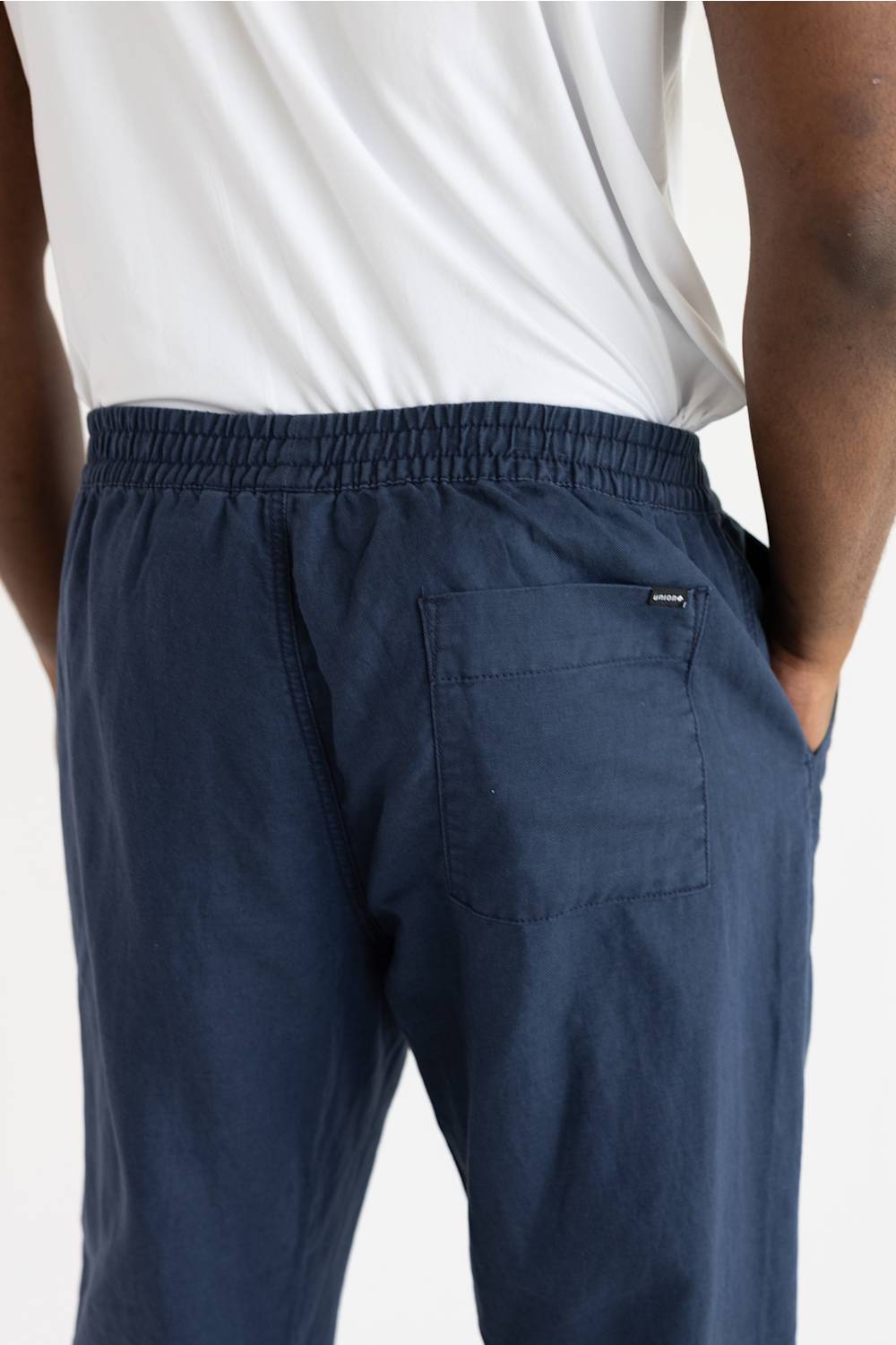 Close-up back view of a person wearing navy blue drawstring lounge pants with a back pocket, paired with a white top against a plain light background.