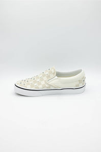 A single slip-on platform sneaker in off-white and cream checkerboard canvas, embellished with metal studs across the toe box, set against a plain light gray background.