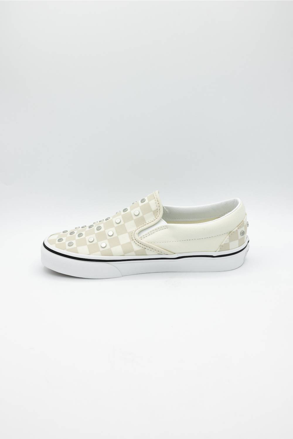 A single slip-on platform sneaker in off-white and cream checkerboard canvas, embellished with metal studs across the toe box, set against a plain light gray background.