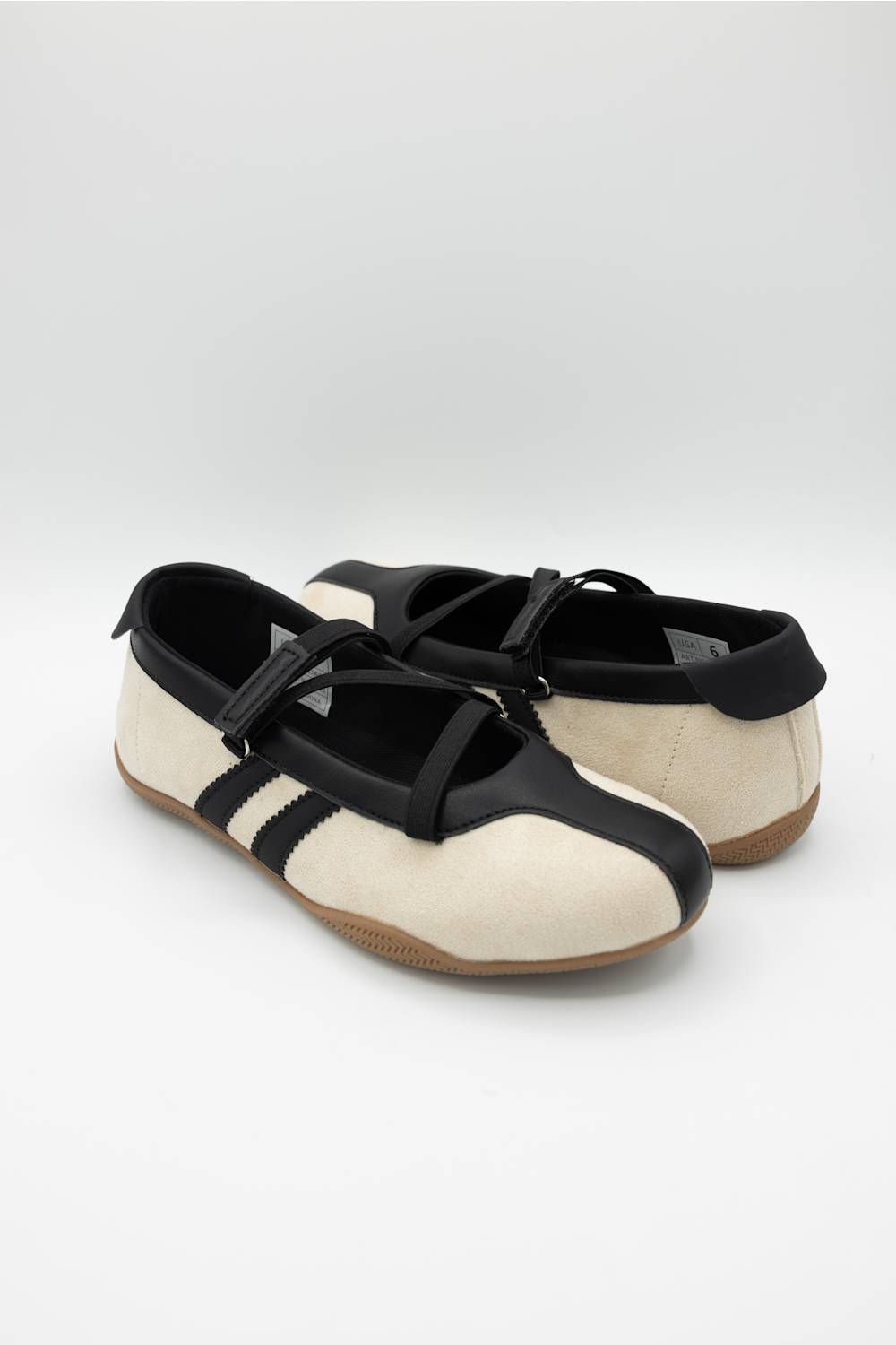 A pair of Mary Jane style shoes with a cream colored upper, black leather trim and strap, and a brown gum sole, shown against a plain light gray background.