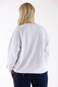Back view of a blonde woman wearing an 1897 Active Falalala Patch Embroidered Fleece Sweatshirt for Women in Ice Grey and dark blue holiday-patterned lounge pants.