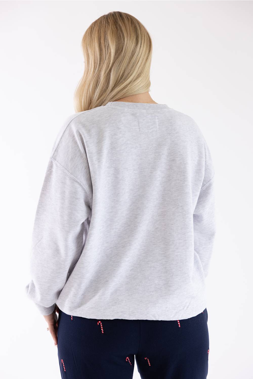 Back view of a blonde woman wearing an 1897 Active Falalala Patch Embroidered Fleece Sweatshirt for Women in Ice Grey and dark blue holiday-patterned lounge pants.
