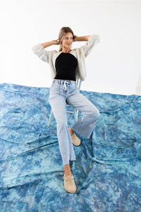 A woman modeling a light gray knit cardigan with a button-up front and drawstring detail, paired with light blue jeans against a plain white background.