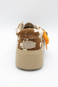 A single platform sneaker shown from the back, featuring a brown and white cowhide upper with a beige rubber sole and an orange braided accent hanging from the side.