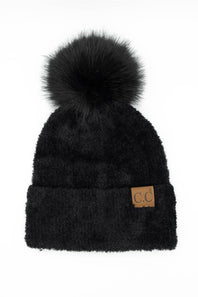 Front view of a black plush pom-pom beanie featuring a cuffed hem with a C.C. branded leather patch, set against a plain white background.