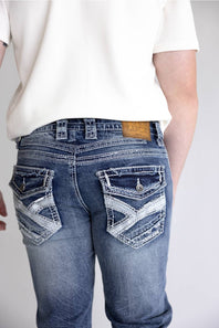 Rear view of a person wearing blue denim jeans with decorative distressed stitching and patch pockets, paired with a white ribbed short-sleeve top against a light gray background.
