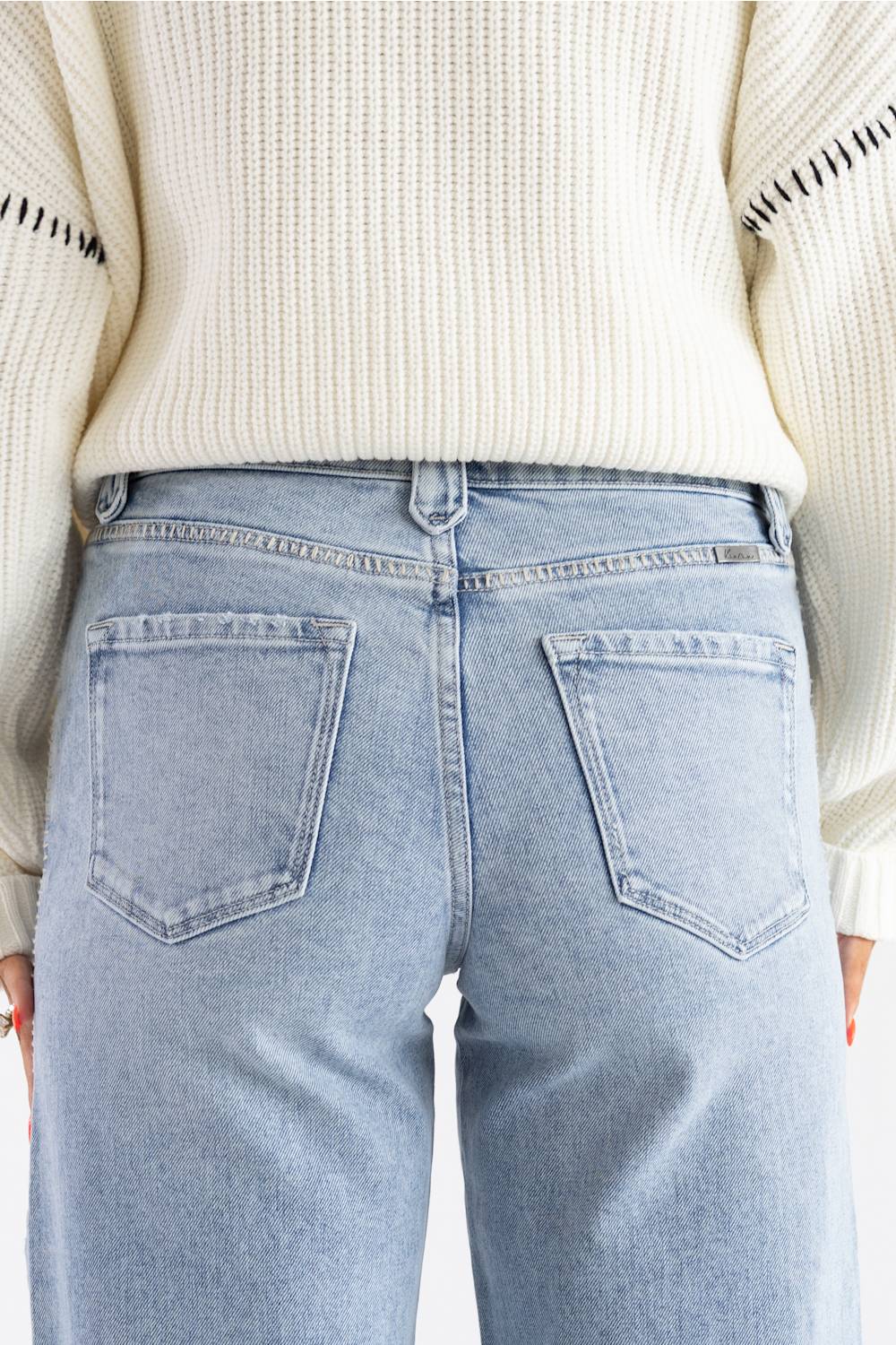 Back view of a person wearing light-wash blue jeans and a cream ribbed knit sweater, cropped from the chest down.