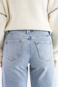 Back view of a person wearing light-wash blue jeans and a cream ribbed knit sweater, cropped from the chest down.