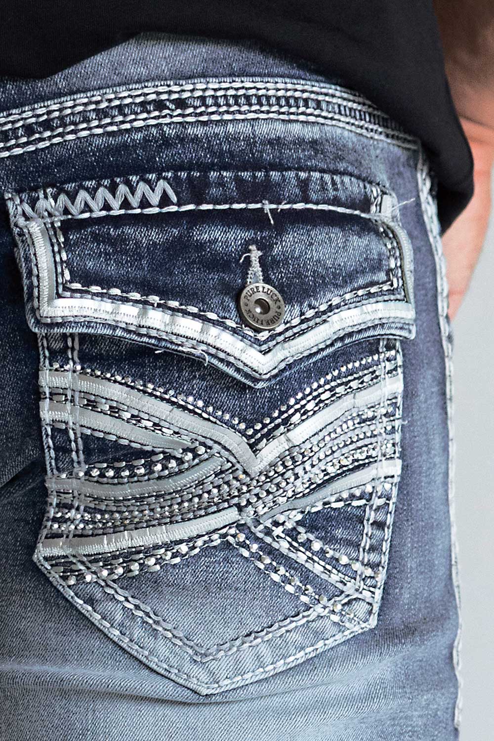 Close-up of the back pocket of distressed blue denim jeans with decorative contrast stitching, a metal button, and a small hanging charm.
