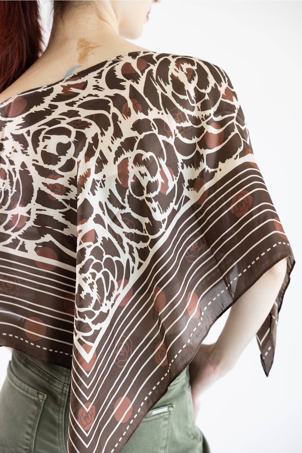 A close-up of a model wearing a brown and cream floral scarf draped over her shoulders, paired with olive green pants against a plain white background.