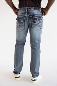 Rear view of a person wearing light-wash blue denim jeans with decorative stitching and silver-toned hardware on the back pockets, paired with a dark top and white sneakers.