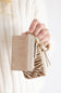 A hand holding a small beige faux-leather card holder and zip pouch set with gold-tone hardware, shown against a soft white knit sweater background.