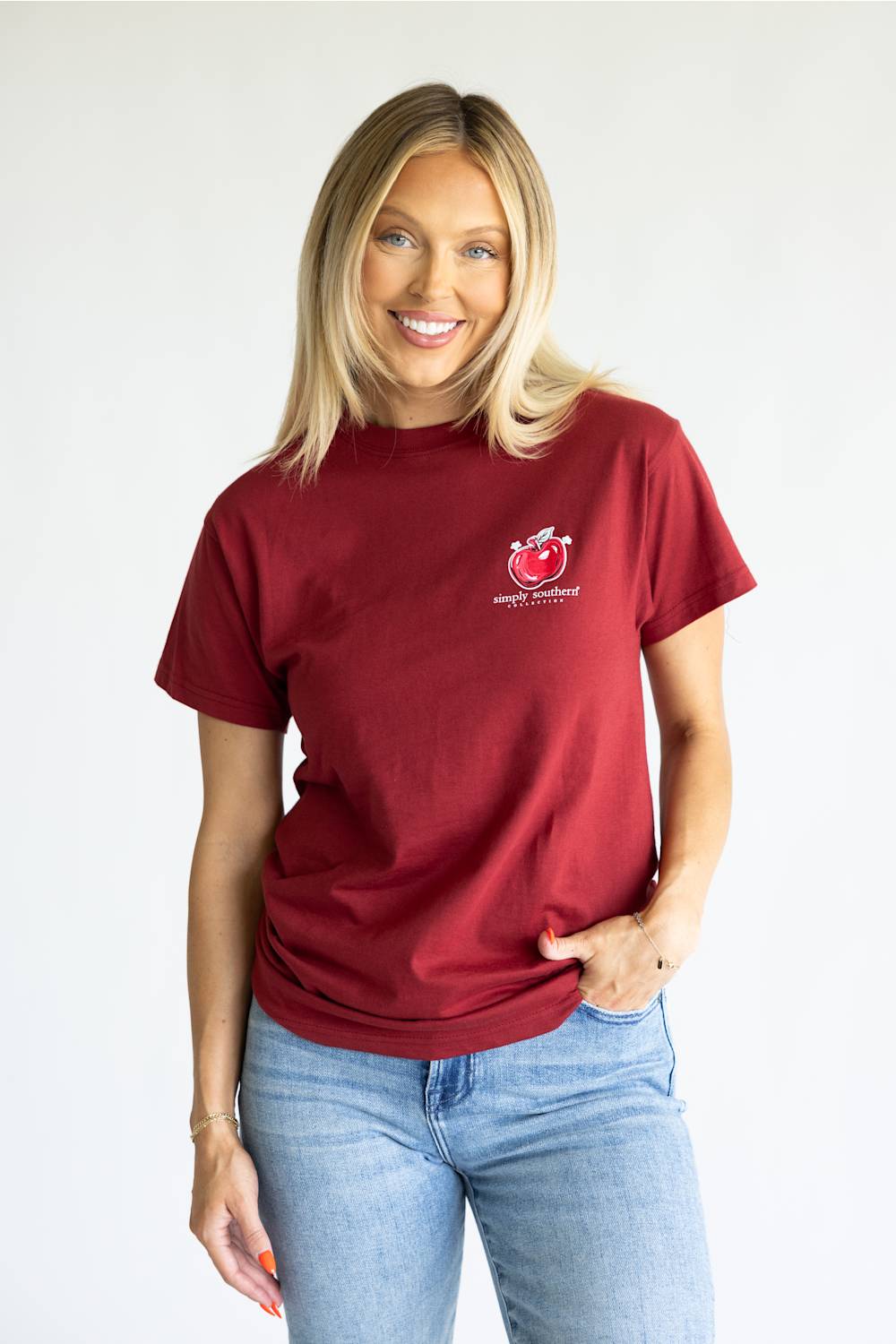 A red short-sleeve t-shirt with a large graphic print on the back, featuring a pink scalloped border, a yellow pencil, a red apple, and the text 'TEACHING IS A WORK OF ART' and 'simply southern' below it.