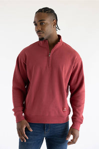 A man wearing a red quarter zip sweatshirt with front pockets and a small red Ariat patch on the left front pocket.