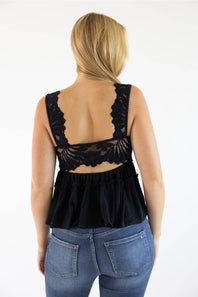 A woman viewed from the back wearing a black lace-trimmed ruffled top and blue jeans against a plain white background.