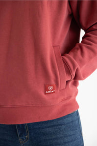 A close up of a man wearing a red quarter zip sweatshirt with front pockets and a small red Ariat patch on the left front pocket.