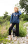 A woman wearing a navy blue crewneck sweatshirt with an embroidered graphic of two mallards and the text 'Suppliers of Quality Outdoors & Apparel'.