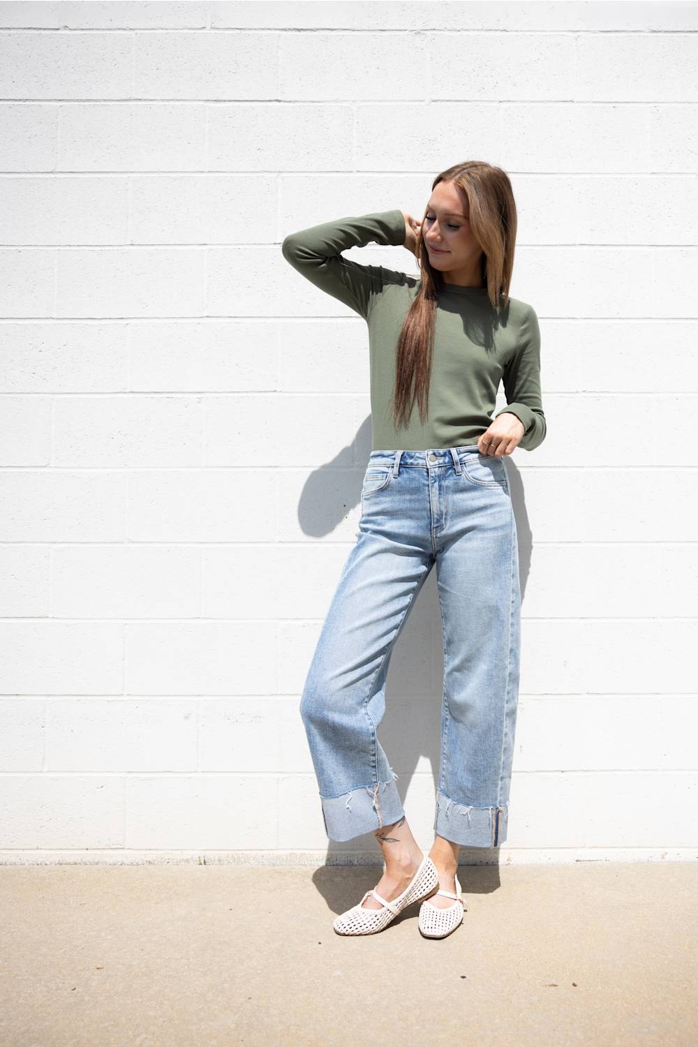 Full-body view of a model in Flying Monkey light-wash barrel leg jeans featuring prominent front side-seam details, thick folded raw-edge cuffs, and high-waist fit against a white brick wall.