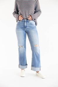 A person wearing cuffed light-wash blue distressed jeans with a striped long-sleeve top and white slip-on shoes, standing against a plain white studio background.