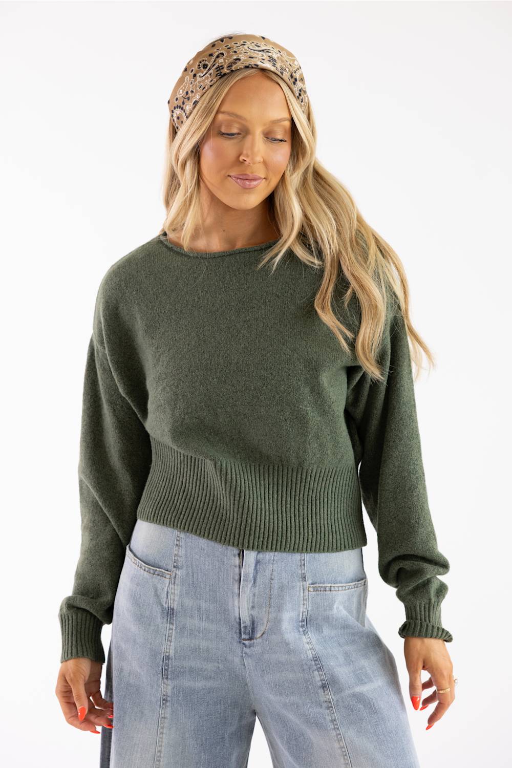 Front view of a model in an olive green knit boat neck sweater paired with light wash denim jeans and a paisley bandana headband.