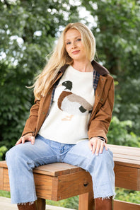 A woman wearing a cream-colored knit sweater with a detailed duck motif on the front
