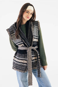 Front view of a model with long dark hair wearing a solid cream fabric boho bandeau headband across her forehead, paired with an olive long-sleeve sweater and patterned fringe vest.
