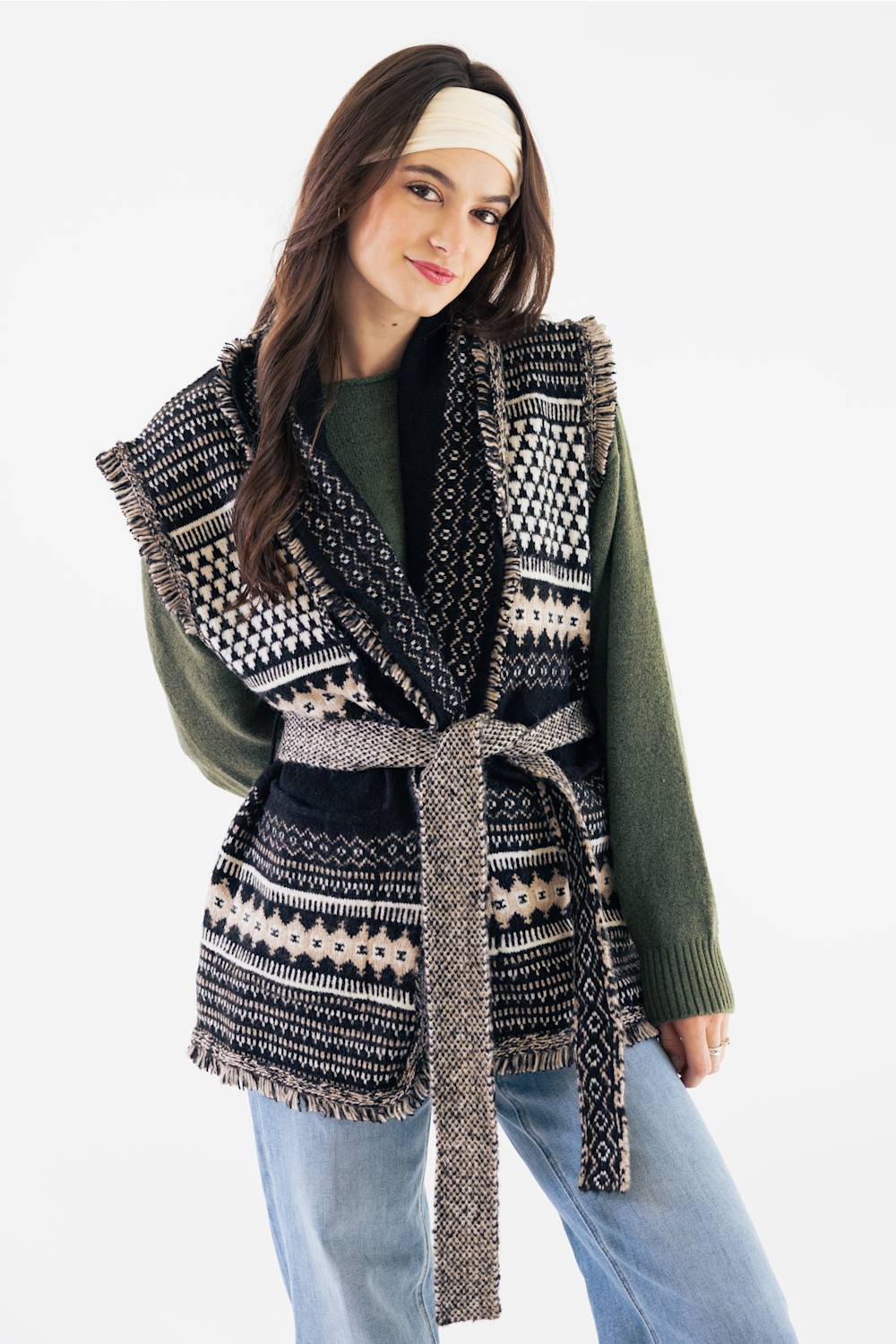 Front view of a model with long dark hair wearing a solid cream fabric boho bandeau headband across her forehead, paired with an olive long-sleeve sweater and patterned fringe vest.
