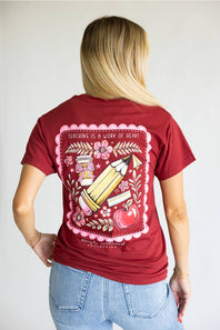 A red short-sleeve t-shirt with a large graphic print on the back, featuring a pink scalloped border, a yellow pencil, a red apple, and the text 'TEACHING IS A WORK OF ART' and 'simply southern' below it.