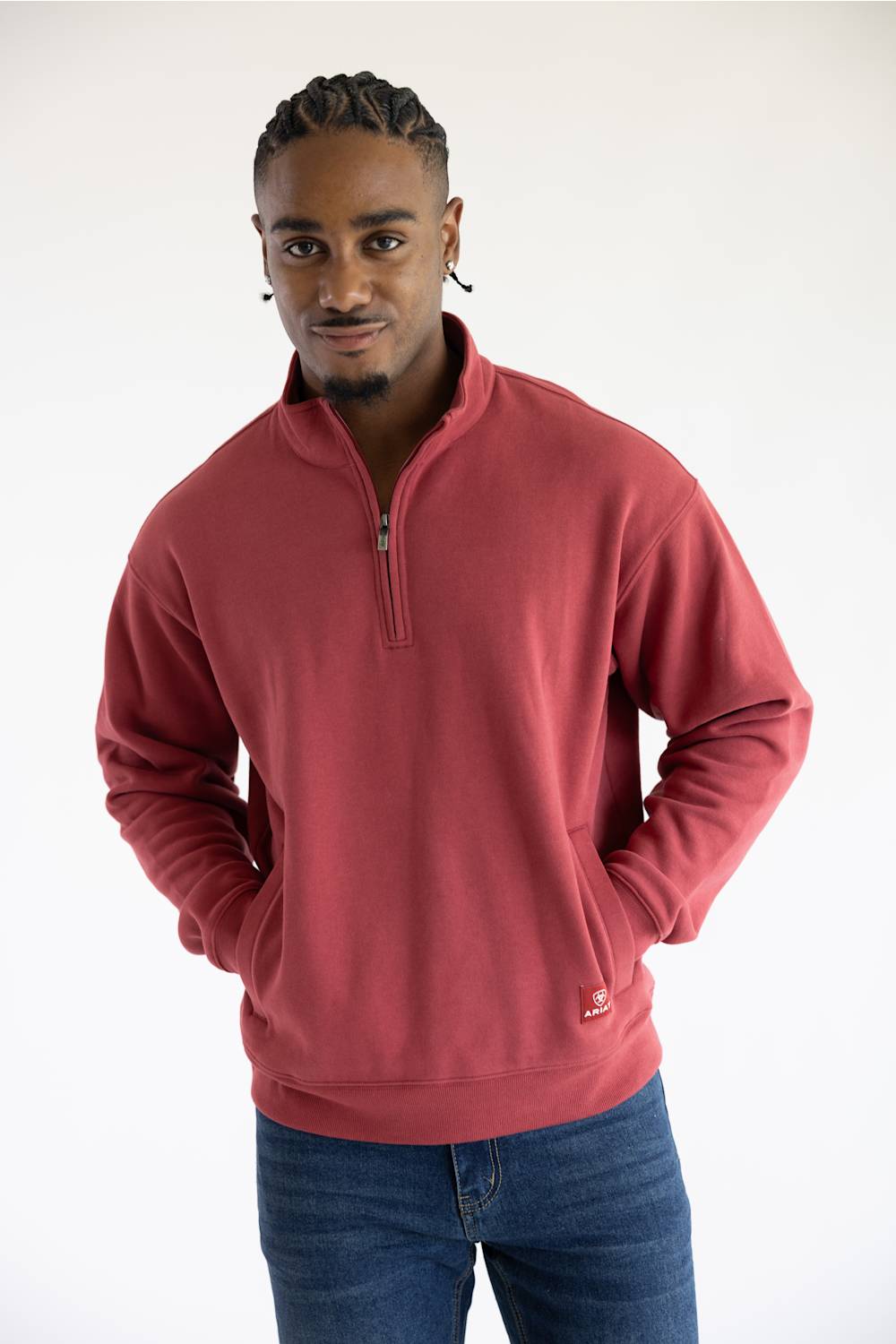 A man wearing a red quarter zip sweatshirt with front pockets and a small red Ariat patch on the left front pocket.