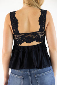 A woman shown from the back wearing a black lace and ruffle sleeveless top with blue jeans against a plain white background.