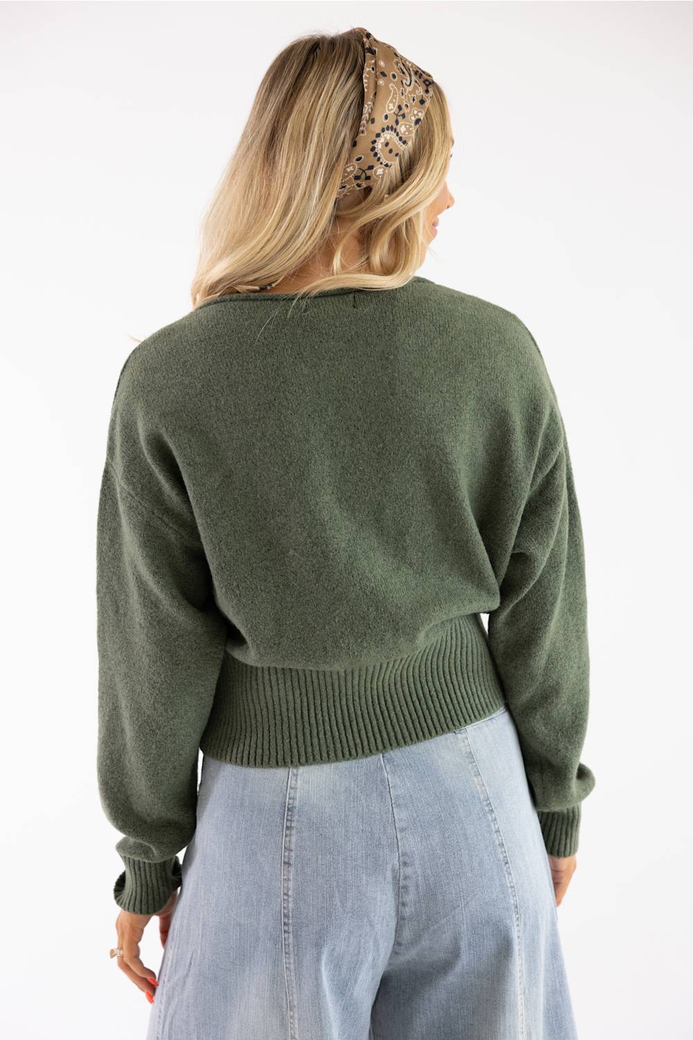 Rear view of a model in an olive green boat neck sweater paired with light wash denim jeans and a patterned headband.