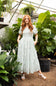 Smocked Floral Maxi Dress for Women in Ivory/Green; Woman in a floral dress standing among plants in a greenhouse