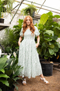 Smocked Floral Maxi Dress for Women in Ivory/Green; Woman in a floral dress standing among plants in a greenhouse