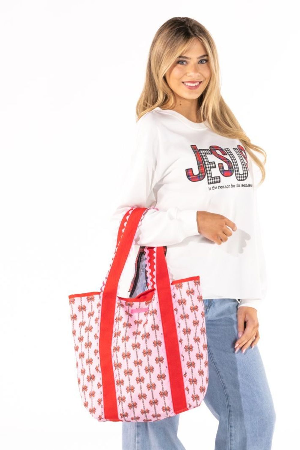 A woman modeling a white long-sleeve sweatshirt with a red and black graphic print, paired with light blue jeans and carrying a white tote bag with red handles and a red and white pattern.