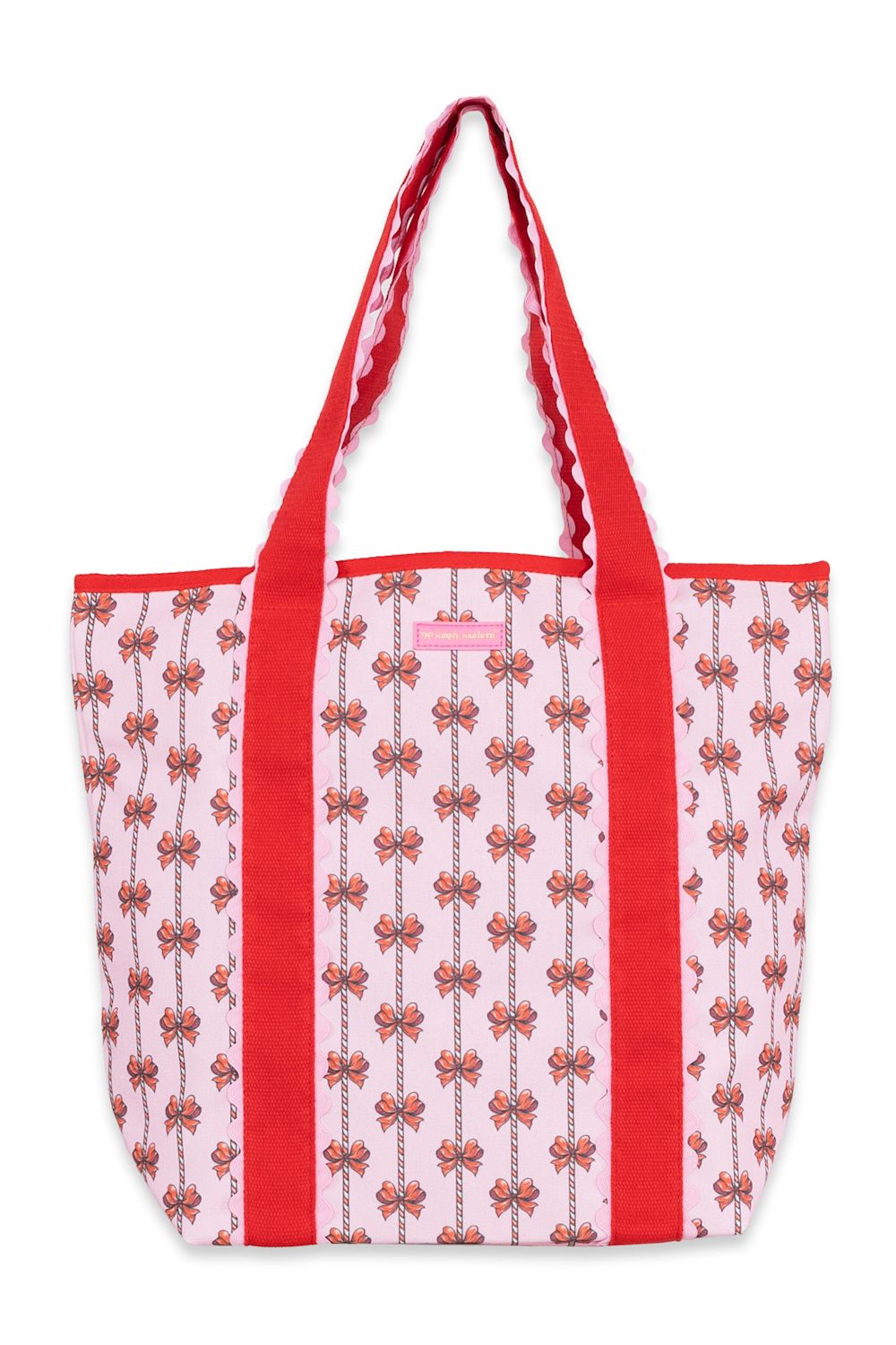 A pink canvas tote bag with red handles and red side panels, decorated with a repeating vertical pattern of small red bows and floral motifs.